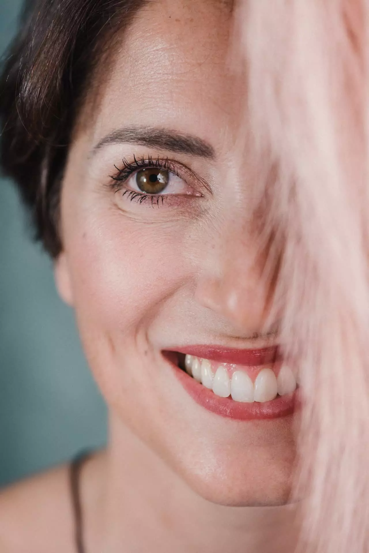 Primo piano di ragazza sorridente con i capelli corti e una piuma rosa davanti al viso